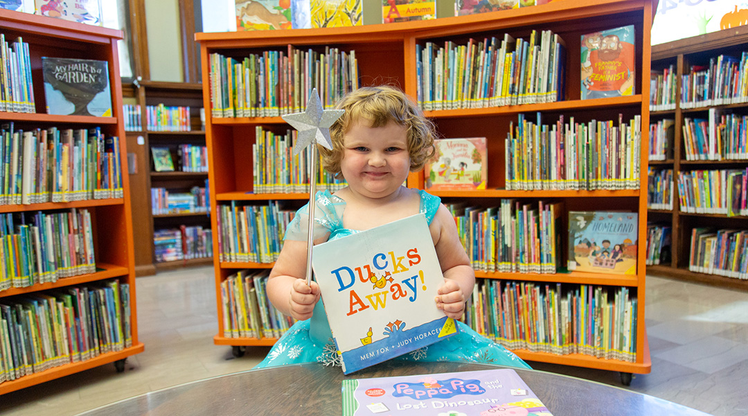 Little girl with a silver wand holding a book up in the Children's Department